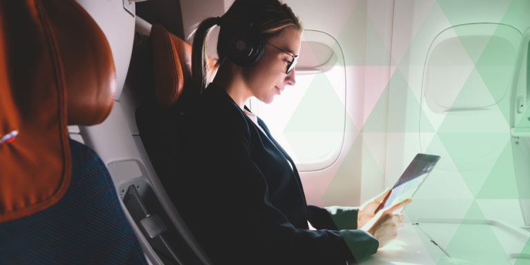 A formally dressed lady sitting inside a plane while looking at a tablet she's holding.